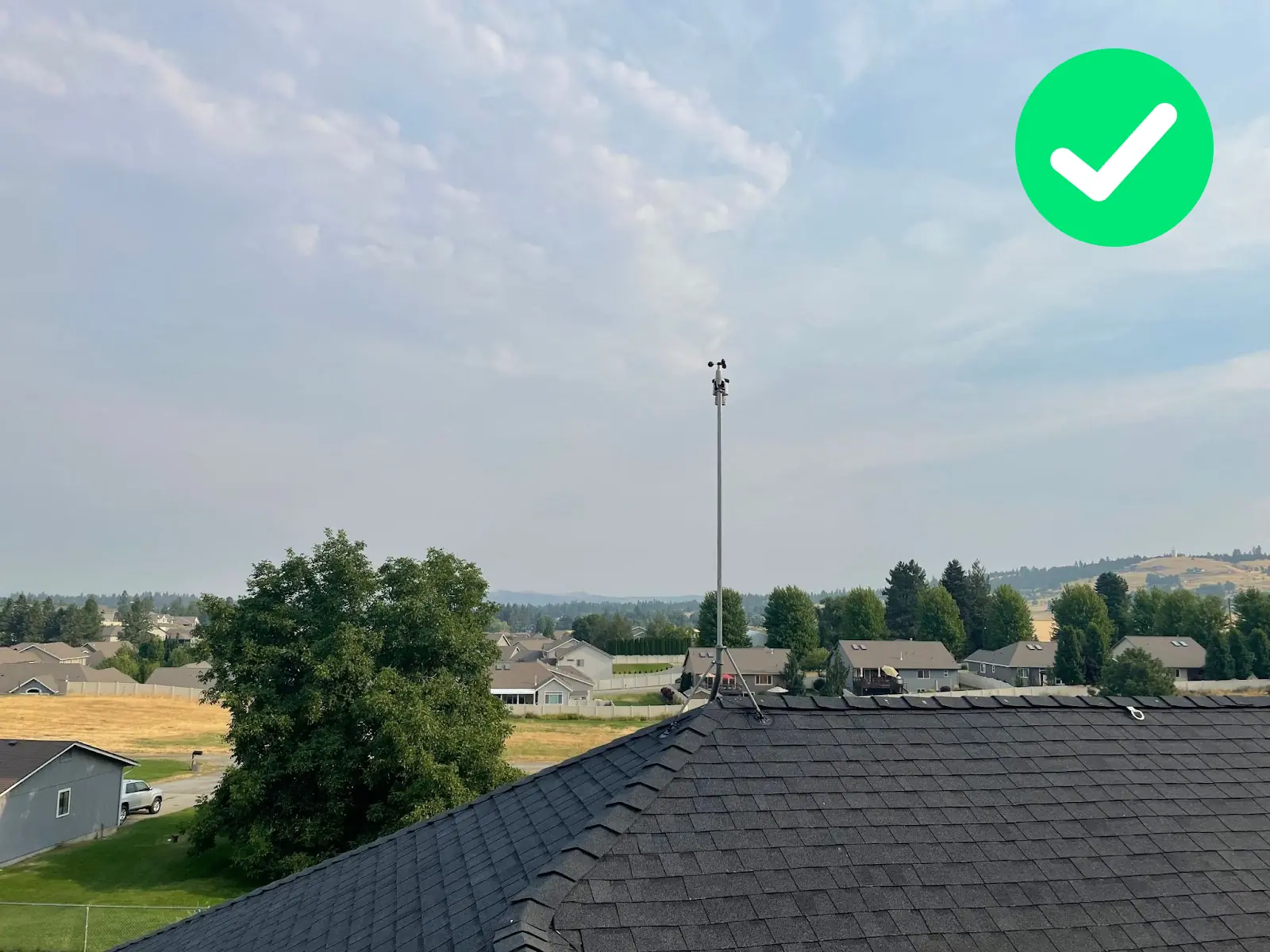 WeatherXM station on a rooftop with a clear horizon and nearby trees below sensor level